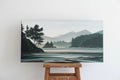 A Fiona Dalrymple painting called Calm Waters - a horizontal landscape painting of a calm lake with mountains, trees, and a shoreline, displayed on a rustic wooden mantel against a white wall.