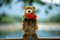 Plush bear holding a salmon in its mouth, with a blurred natural background