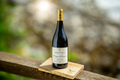 Noble Ridge pinot noir wine bottle on a wooden coaster with a blurred natural background