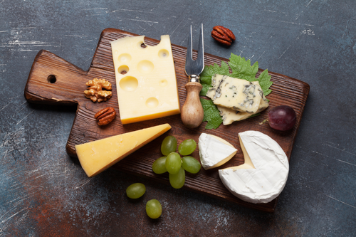 Assorted cheeses on a wooden board with grapes and nuts on a dark surface