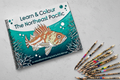 Coloring book titled 'Learn & Colour The Northeast Pacific' with fish illustration on a wooden surface, accompanied by colored pencils.