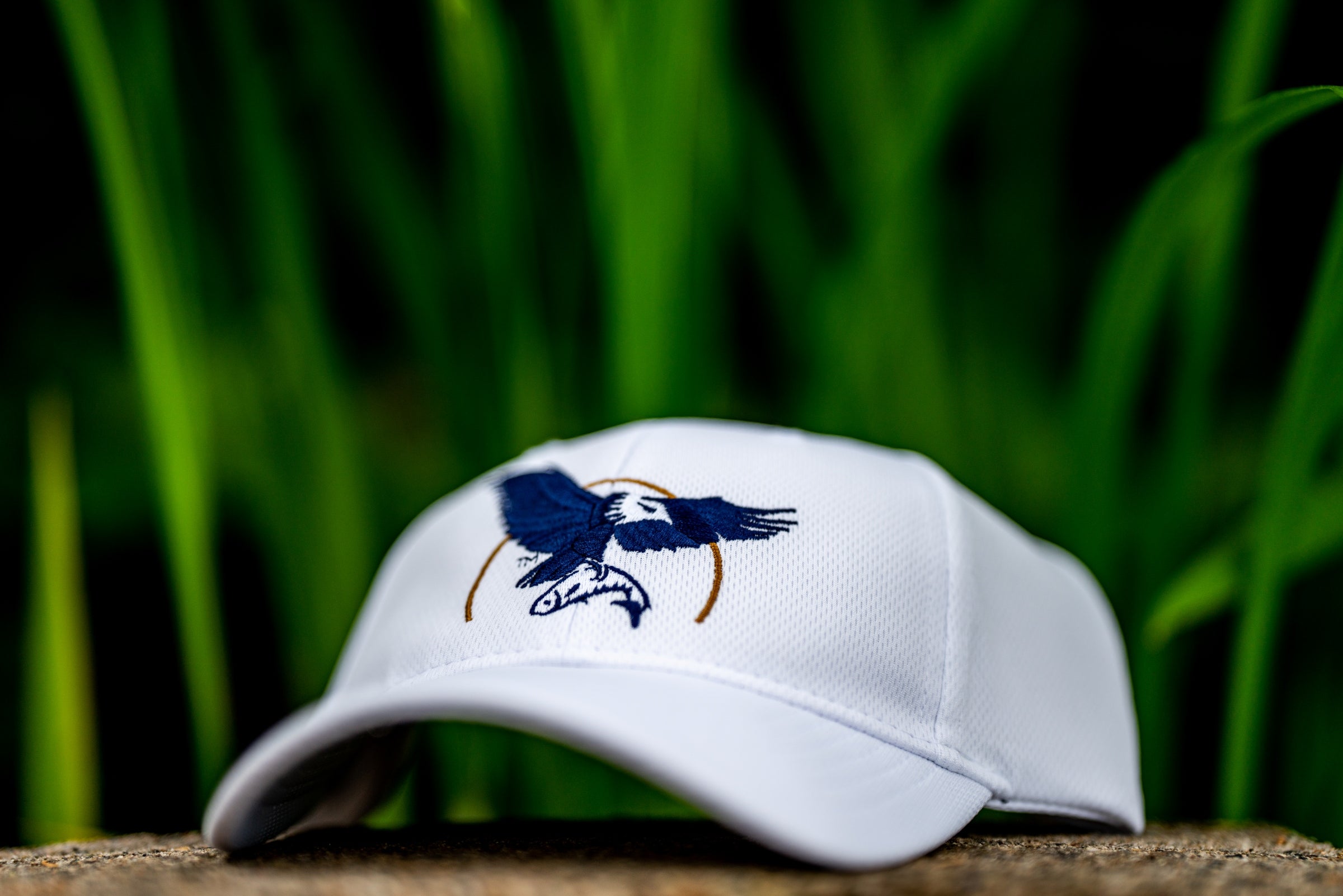 White cap with a blue eagle logo on a wooden surface with green grass in the background