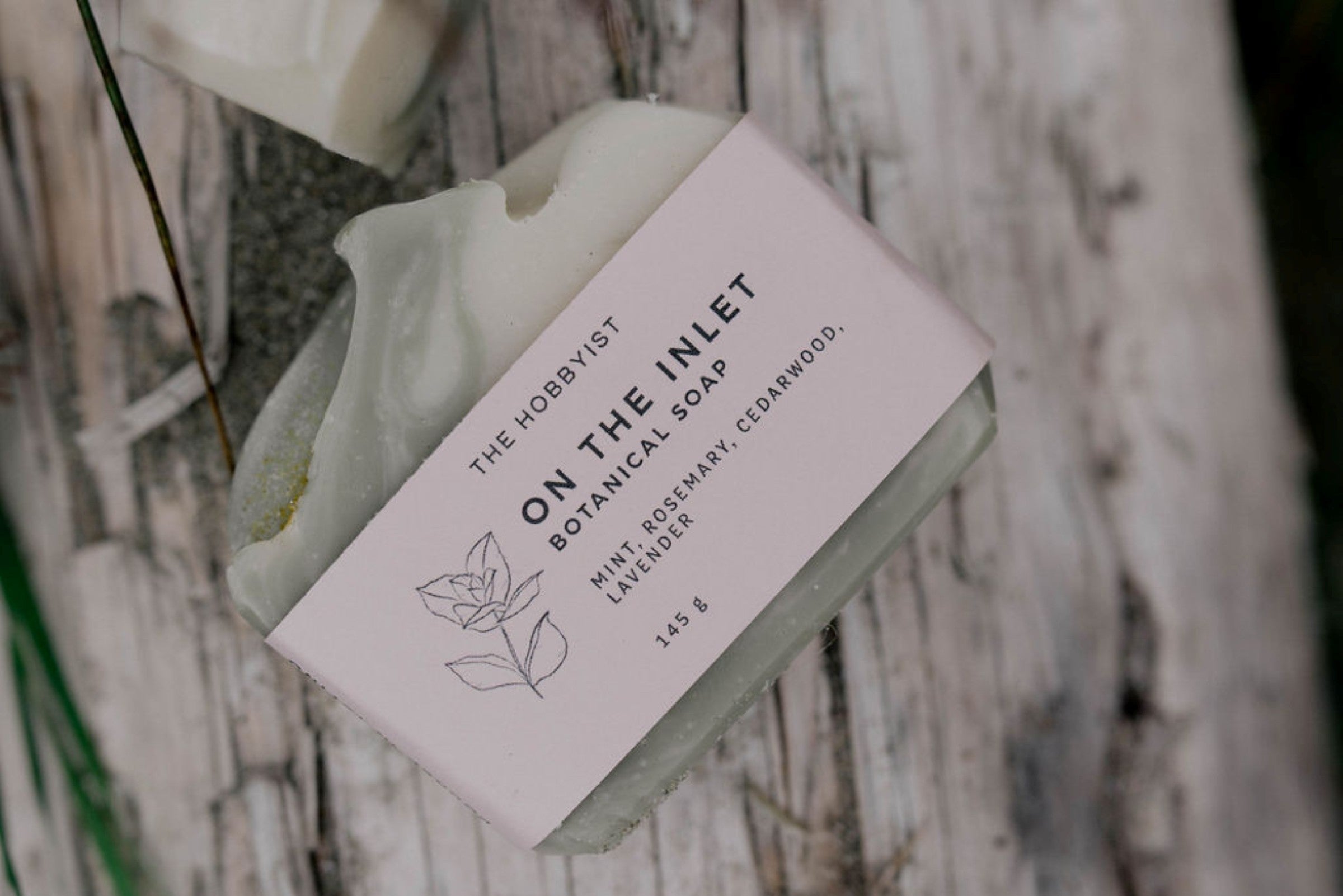 The Hobbyist On The Inlet Botanical Soap. Mint, Rosemary, Cedarwood, Lavender. 145g. on a wood surface.
